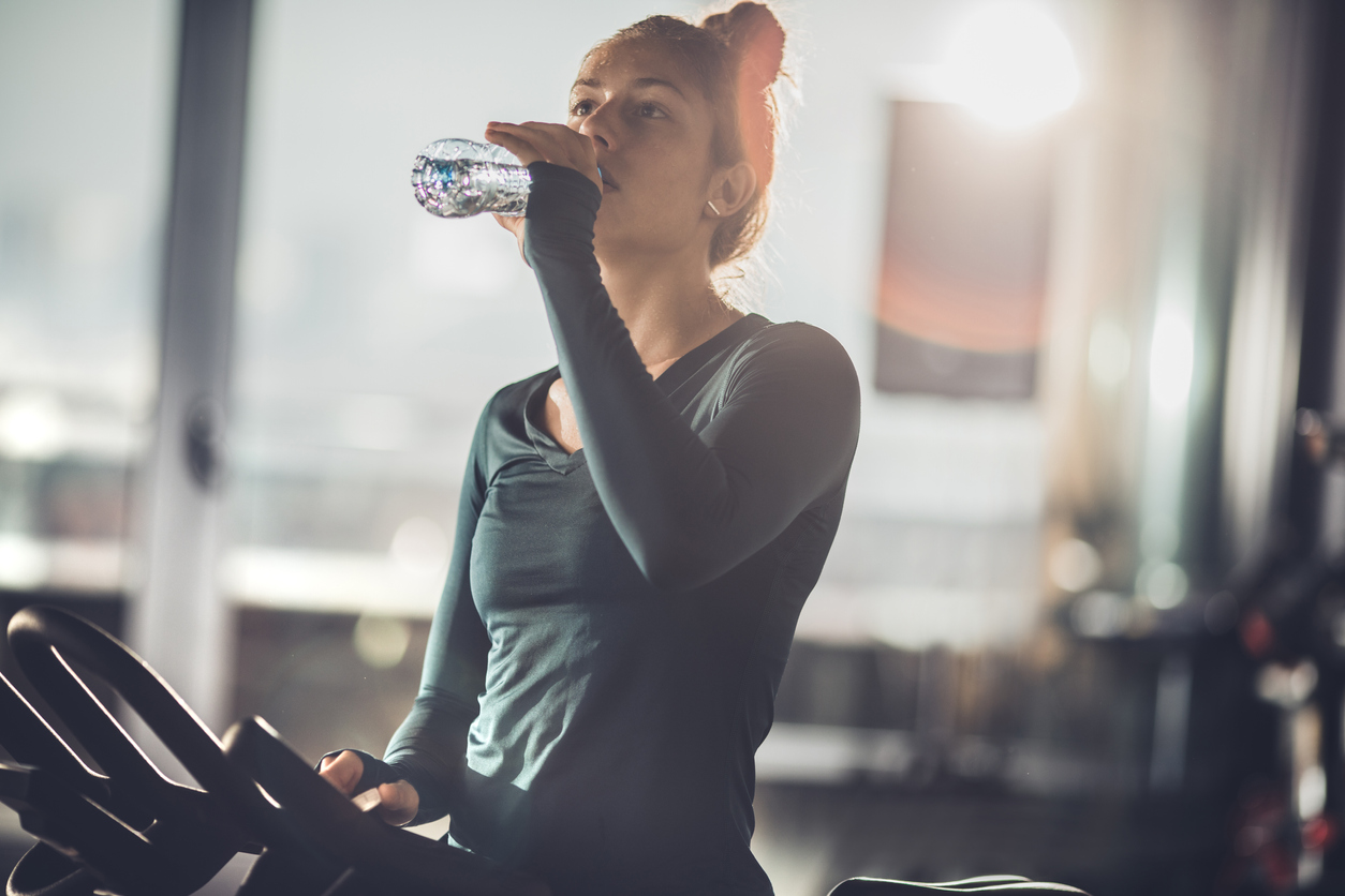 Tired female athlete drinking fresh water while resting from exercising class in a health club.